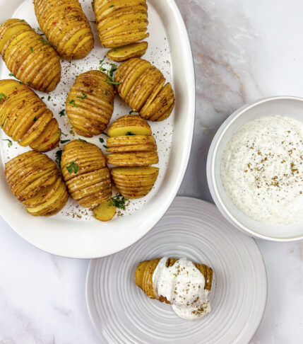 A close-up of a delicious hassle potato dish with creamy yogurt sauce and zaatar seasoning.