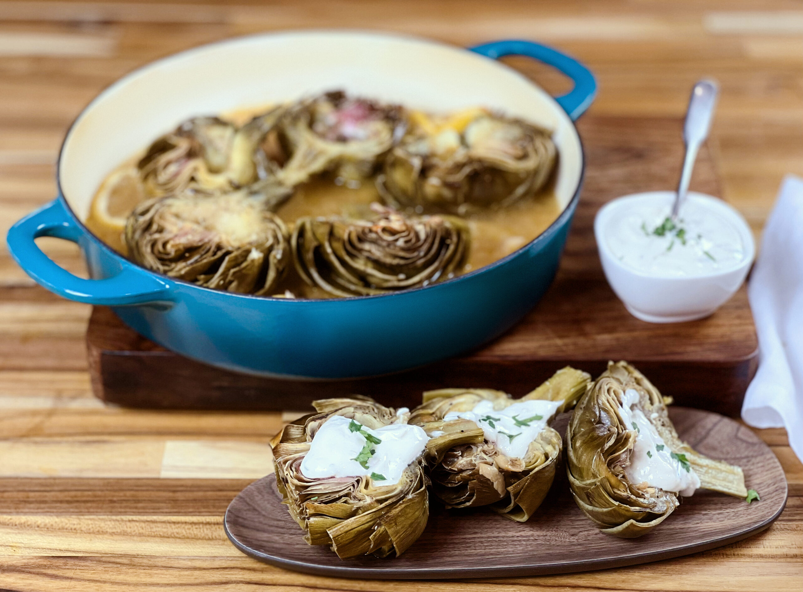 Pan of braised artichoke hearts with a side of dipping sauce