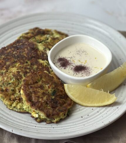 Plate of crispy and golden zucchini fritters with a dollop of creamy tahini sauce on the side.