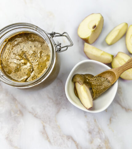 A jar filled with homemade Nutty Bliss Nut Butter accompanied by slices of fresh apples.