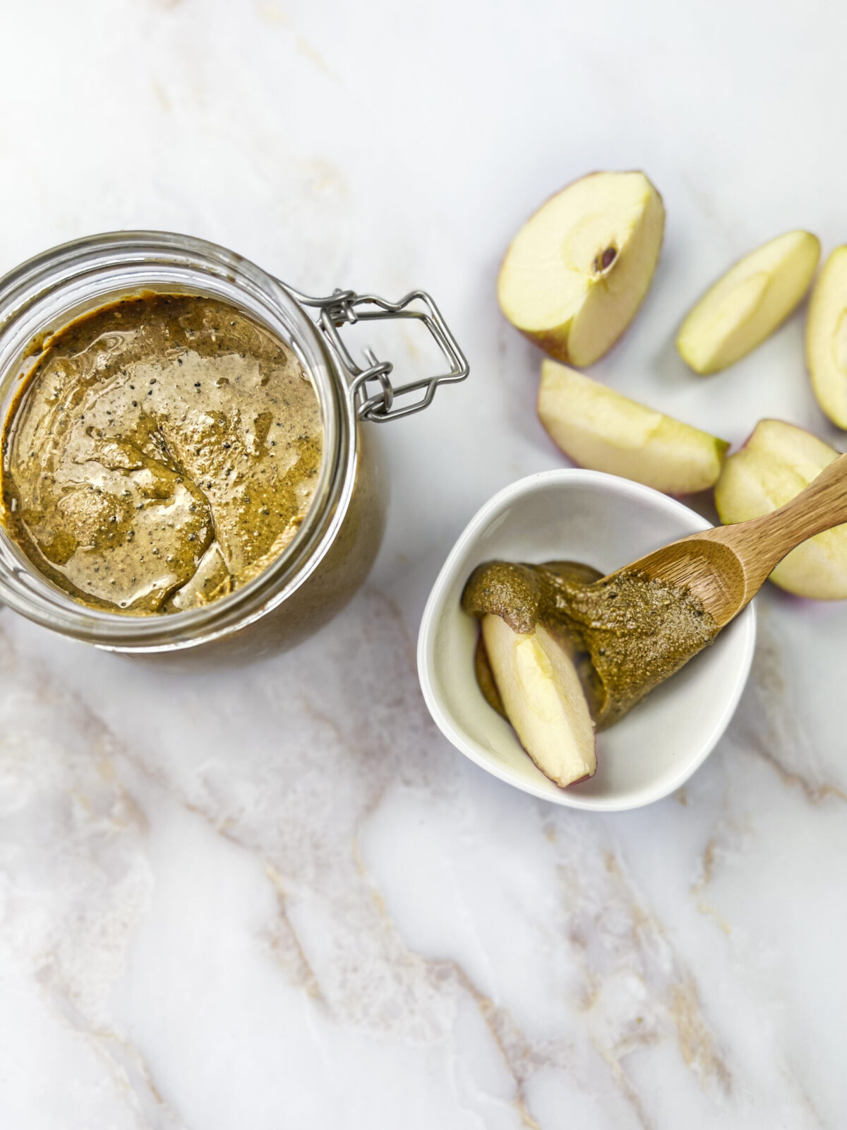 A jar filled with homemade Nutty Bliss Nut Butter accompanied by slices of fresh apples.