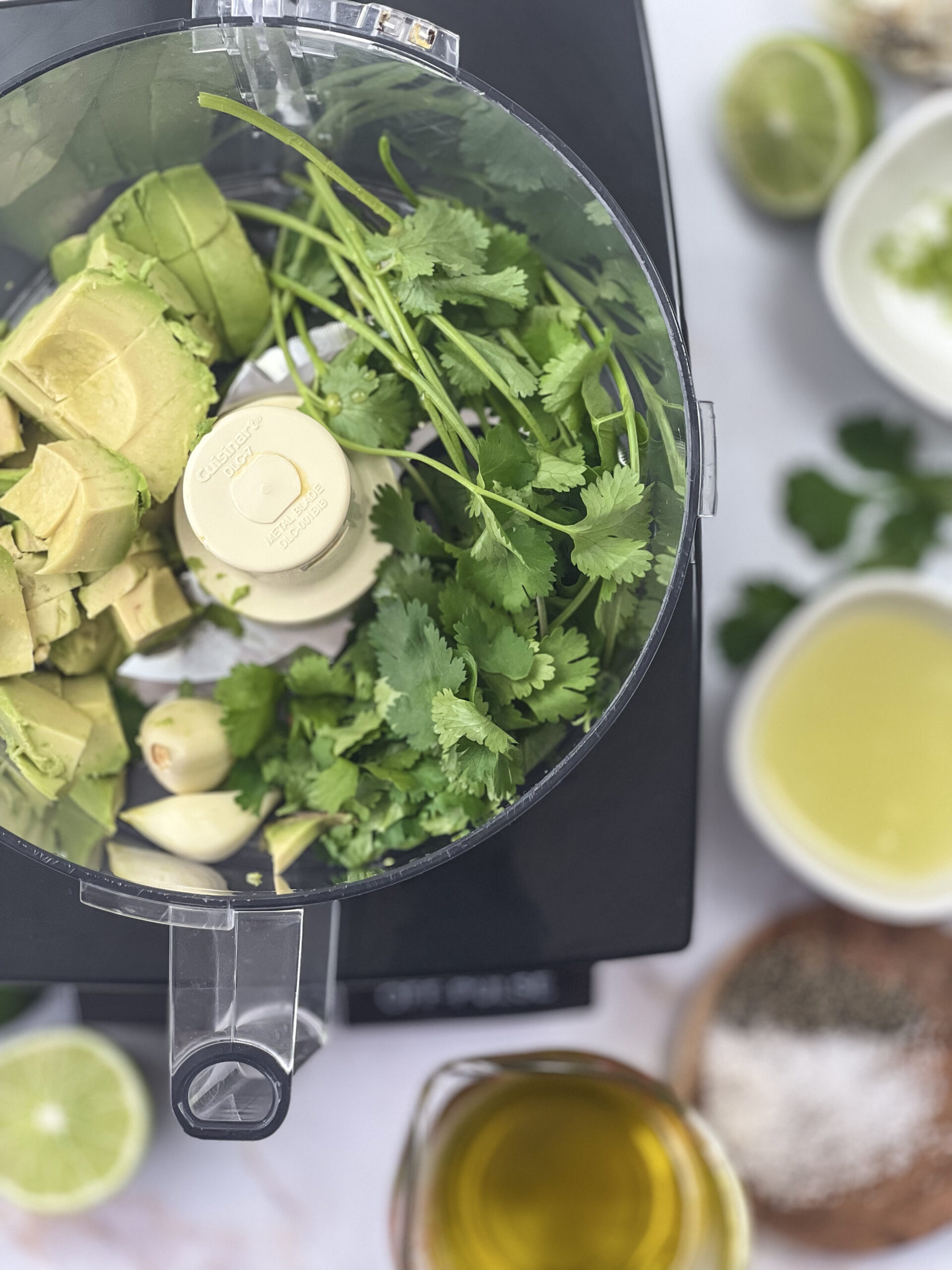 A colorful assortment of diced avocado, minced garlic, lime juice, fresh cilantro, and other ingredients patiently awaiting their turn in the food processor to become the creamy Avocado Lime Dressing.