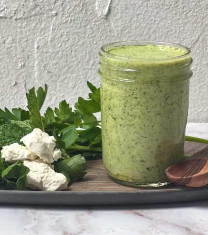 A jar filled with Greek Goddess Salad Dressing and a wooden spoon beside it.