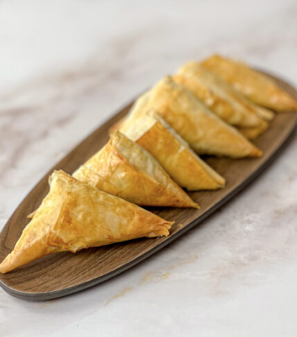 Golden spanakopita triangles served on a plate, ready to eat.