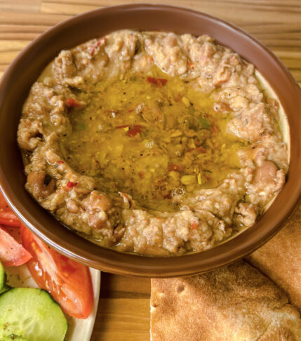 A bowl of Foul Mudammas with pita bread and fresh vegetables.