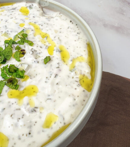 A delicious bowl of creamy yogurt cucumber salad with fresh herbs, diced onions, and a tangy lemon dressing.