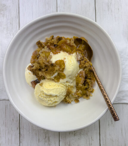 Golden brown peach crisp on a plate with a scoop of melting vanilla ice cream