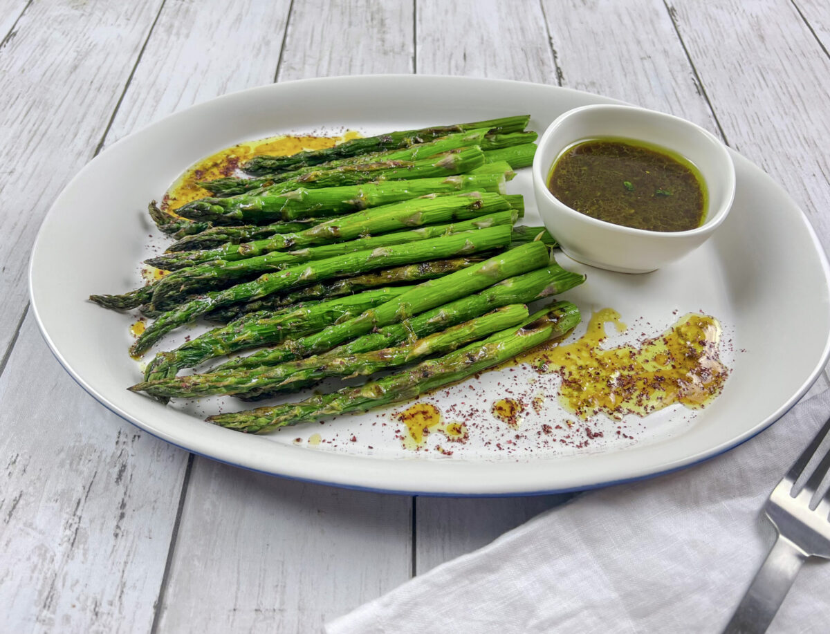 Plate of grilled asparagus spears with a side of pomegranate molasses dressing.