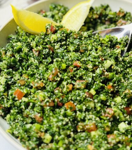 Fresh tabbouleh salad served on a white plate, garnished with lemon wedges and crisp lettuce.