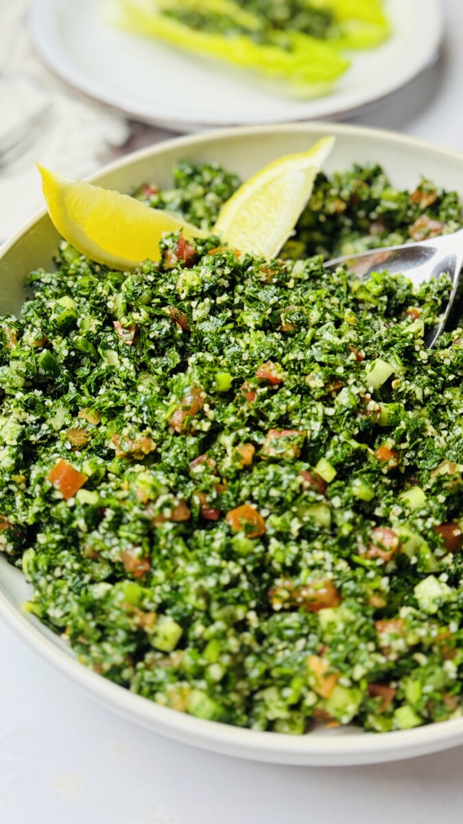 Fresh tabbouleh salad served on a white plate, garnished with lemon wedges and crisp lettuce.