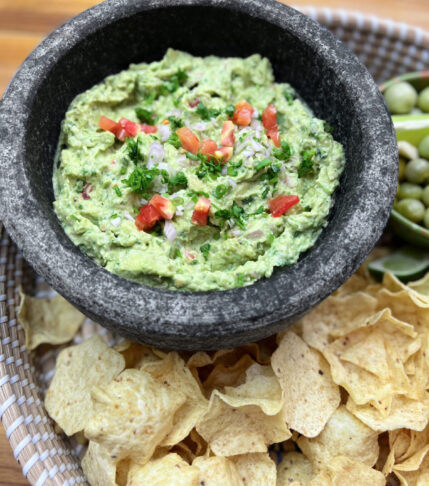 Fresh guacamole in a traditional mortar and pestle with tortilla chips on the side.