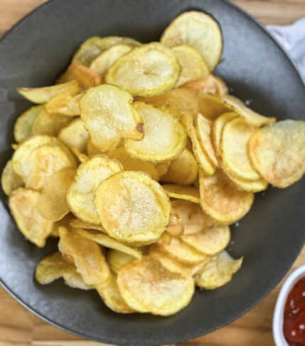 Golden homemade potato chips in a bowl, perfectly crispy and perfectly seasoned. With a bowl of ketchup.