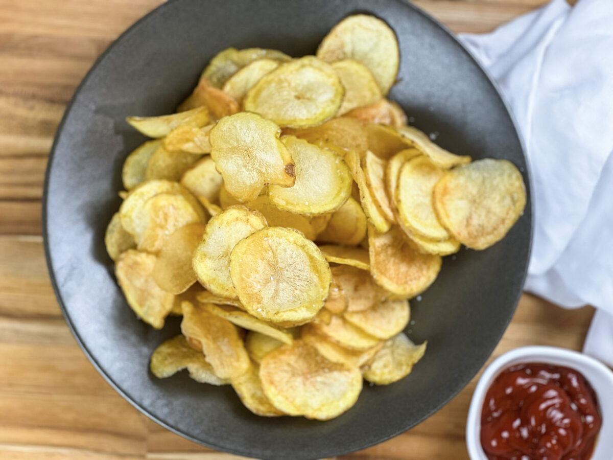 Golden homemade potato chips in a bowl, perfectly crispy and perfectly seasoned. With a bowl of ketchup.