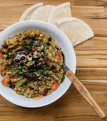 Finished bowl of Baba Ghanoush garnished beautifully, accompanied by fluffy pita bread.