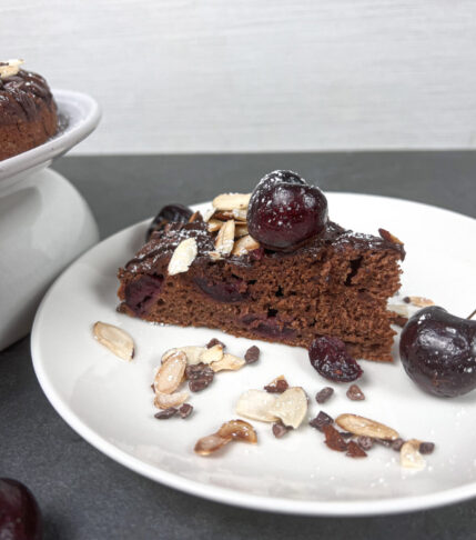 Slice of Chocolate Cherry Cake on a plate with cherries and slivered almonds on top.