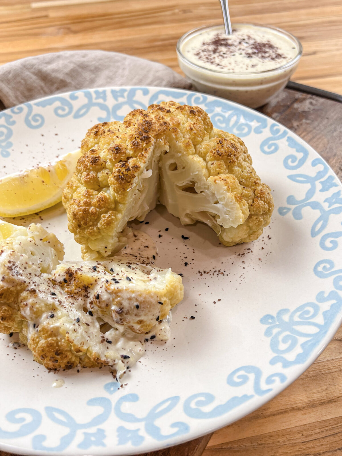 Golden-brown whole roasted cauliflower served with creamy tahini feta sauce, garnished with sumac and nigella seeds.