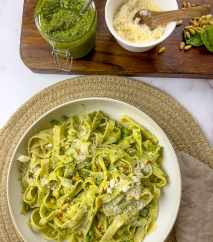 A plate of pasta mixed with fresh homemade pesto sauce, a jar of extra pesto, and a bowl of grated cheese