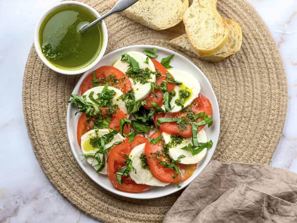 A vibrant Caprese salad on a platter accompanied by a jar of homemade basil oil and fresh bread