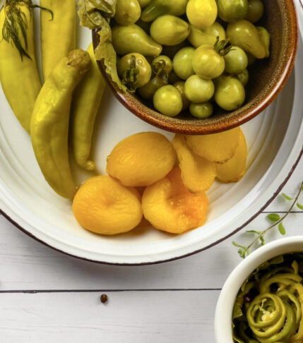 A vibrant platter of pickled banana peppers, pickled green tomatoes, pickle slices, and jalapenos.