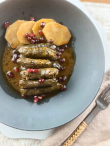 Platter of perfectly rolled stuffed grape leaves with lemon wedges and fresh herbs.