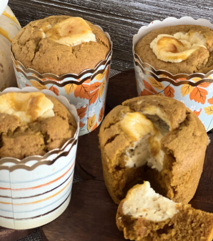 A batch of freshly baked pumpkin cream cheese muffins on a rustic wooden surface.