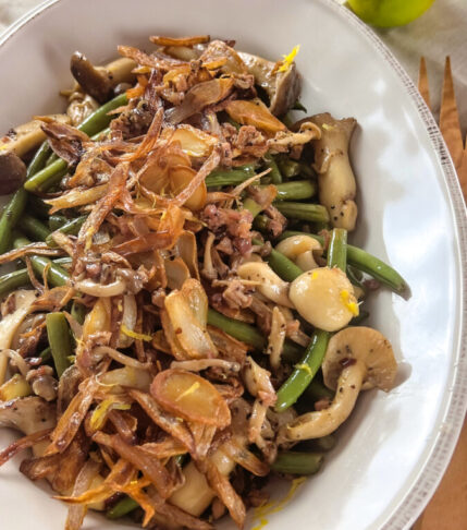 A vibrant plate of sautéed green beans and mixed mushrooms, topped with golden, crispy shallots.