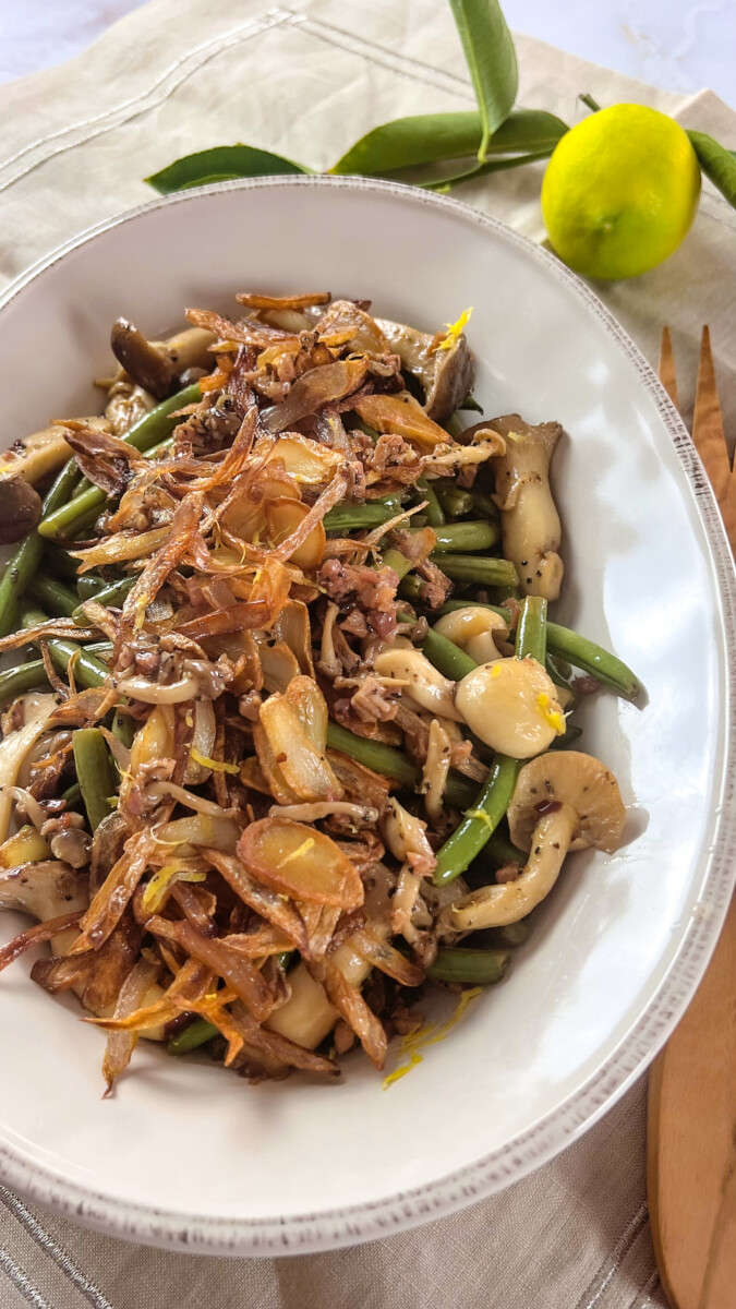 A vibrant plate of sautéed green beans and mixed mushrooms, topped with golden, crispy shallots.