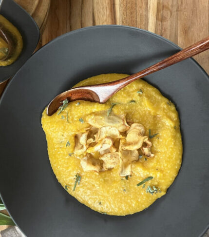 Creamy pumpkin butter polenta in a bowl topped with parsnip chips, toasted pumpkin seeds, and freshly grated parmesan.