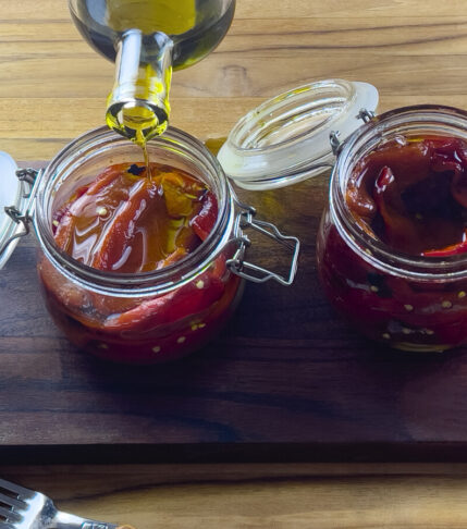 wo glass jars filled with charred bell peppers preserved in olive oil.