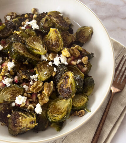 Golden-brown roasted Brussels sprouts drizzled with pomegranate molasses dressing, garnished with vibrant pomegranate seeds on a rustic plate."