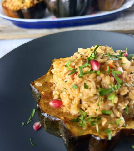 Stuffed acorn squash halves garnished with pomegranate seeds on a rustic serving platter.