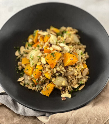 A delicious bowl of pearl farro salad with roasted butternut squash, garnished with toasted almonds, Italian parsley, and barberries.