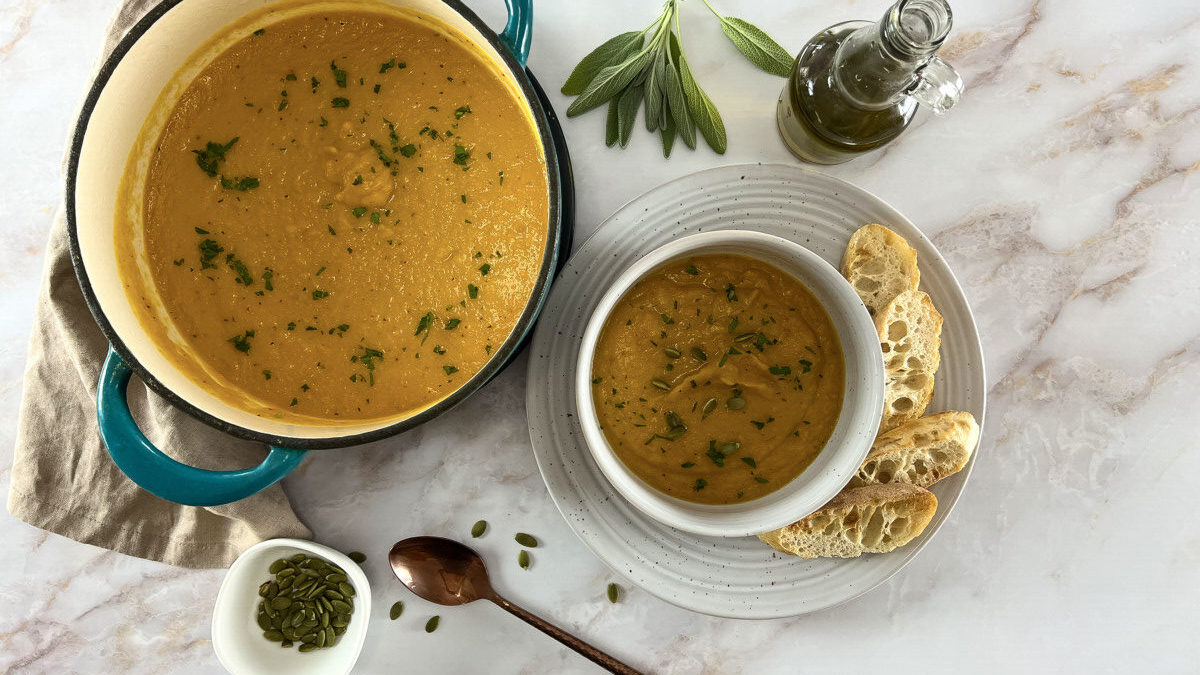 Large pot and bowl of roasted Butter Nut Squash Soup garnished with toasted pumpkin seeds and accompanied by slices of baguette bread