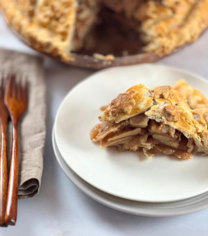 Perfectly easy baked deep-dish apple pie with a golden crust, with one slice served on a plate beside it.