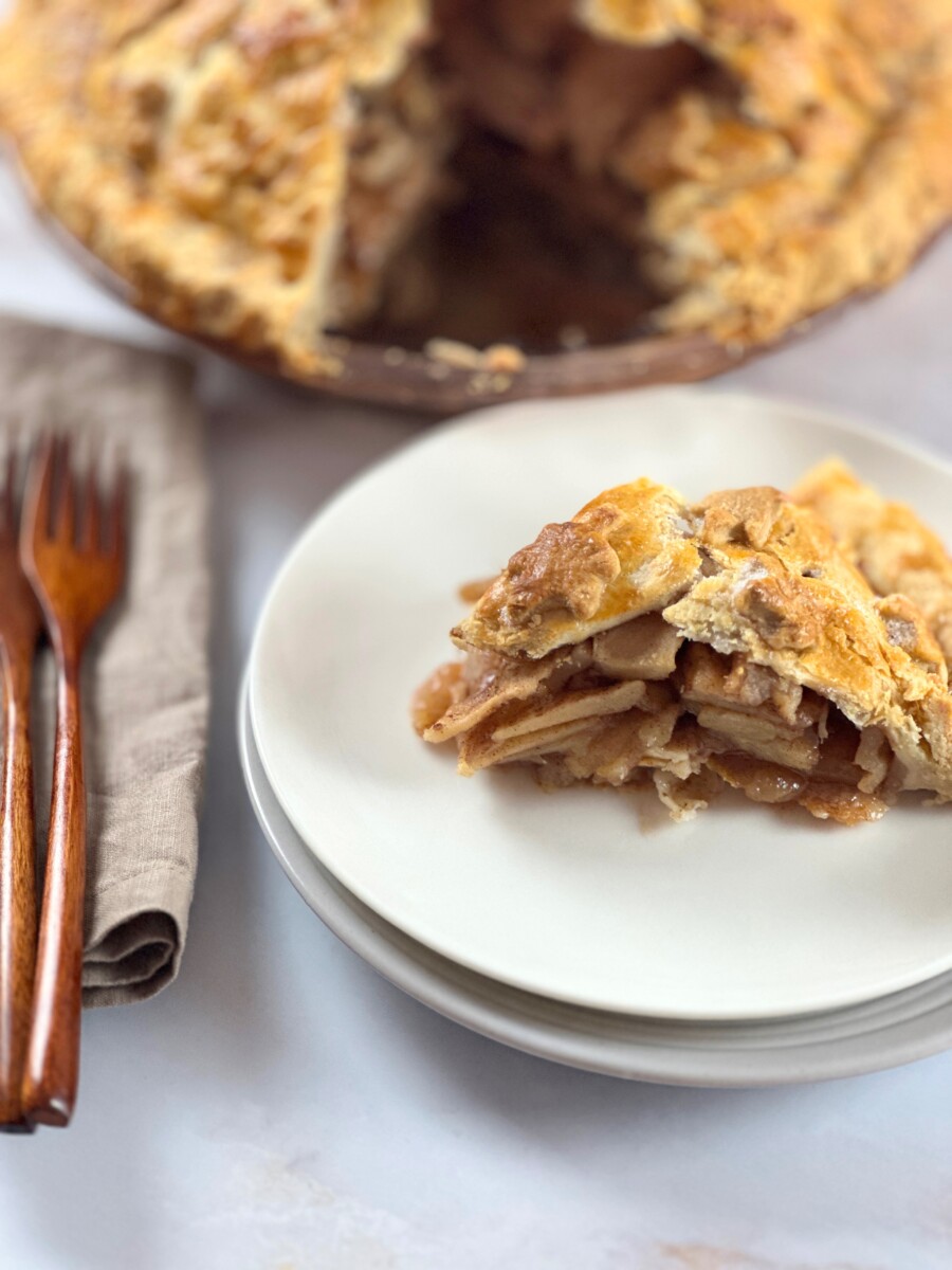 Perfectly easy baked deep-dish apple pie with a golden crust, with one slice served on a plate beside it.