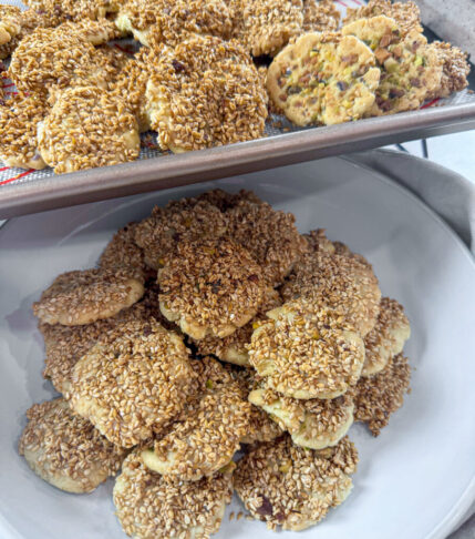 A plate filled with golden Barazek cookies topped with sesame seeds and pistachios.