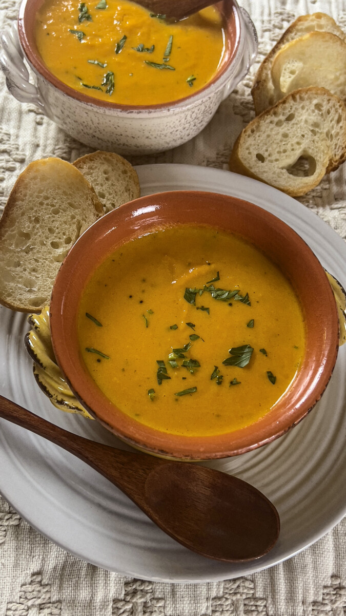 Two bowls of creamy carrot coconut soup accompanied by slices of fresh bread