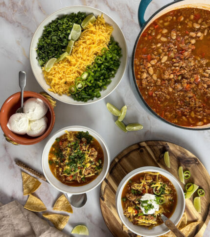 Pot of easy turkey chili alongside two serving bowls and a variety of chili toppings