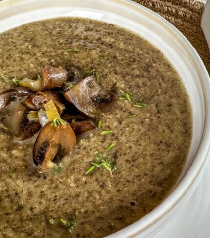 A steaming bowl of vegan cream of mushrooms garnished with fresh herbs.