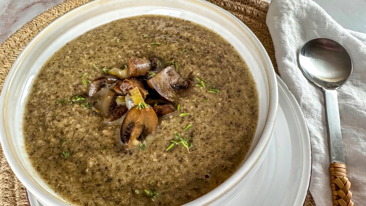 A steaming bowl of vegan cream of mushrooms garnished with fresh herbs.