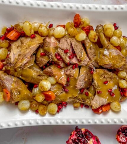 Roasted whole duck sliced on a platter with pearl onions and pomegranate seeds