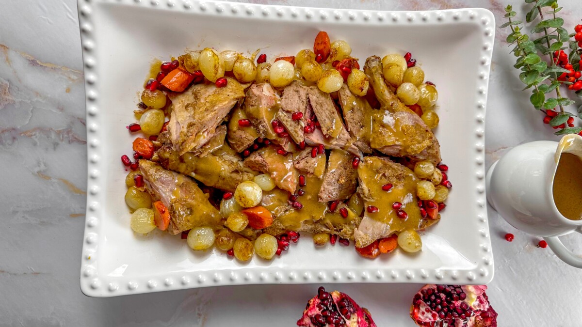 Roasted whole duck sliced on a platter with pearl onions and pomegranate seeds