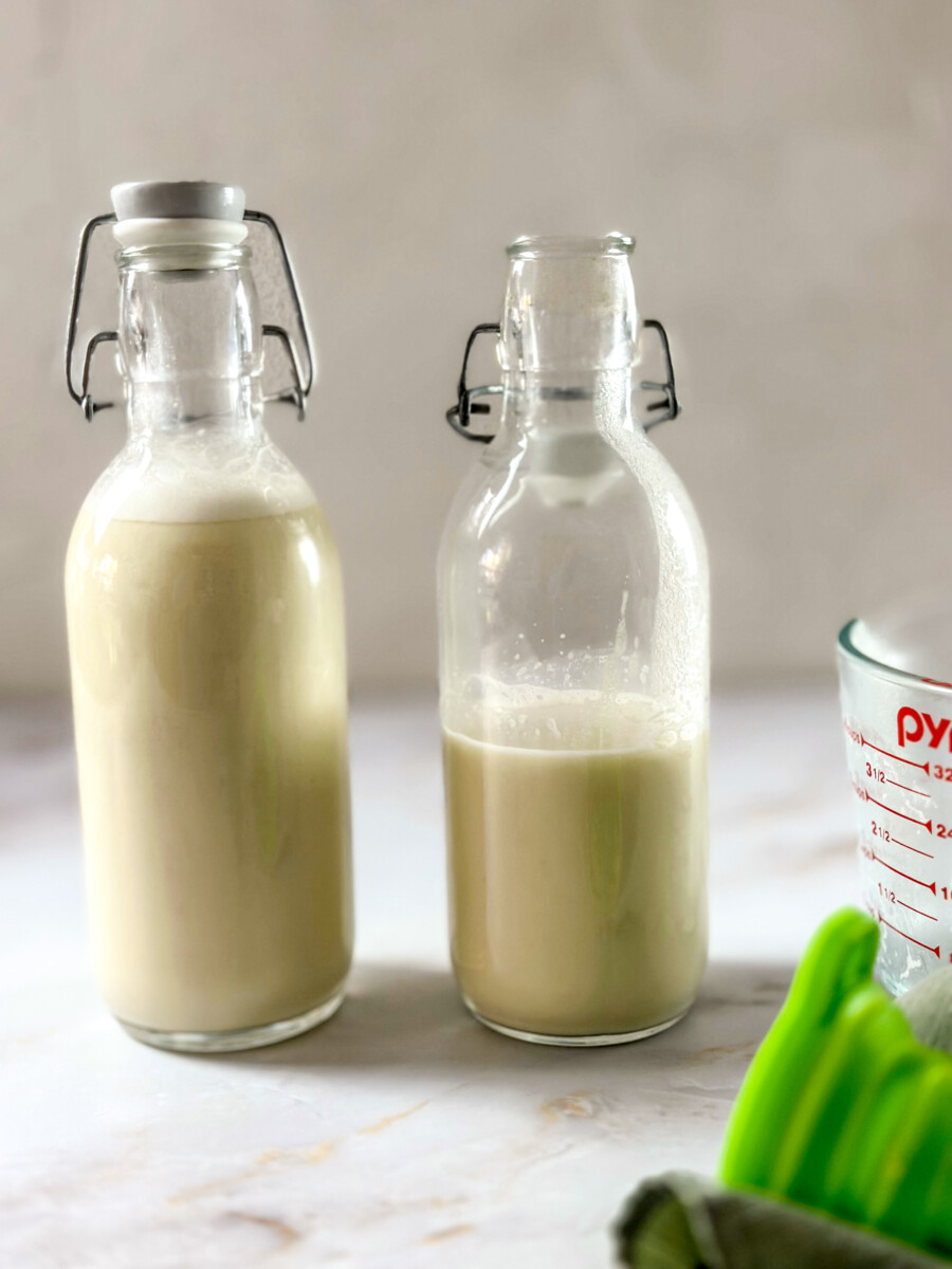 Two bottles of creamy cashew cream, a dairy-free alternative, sitting on a wooden surface.