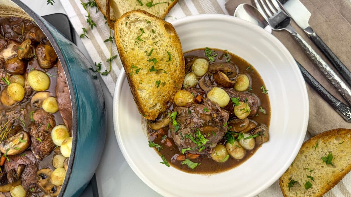 a bowl of Traditional Coq au Vin wit ha sliced of crusty French bread is a classic of French cuisine. This hearty stew exudes the warmth and soul of rural France. 