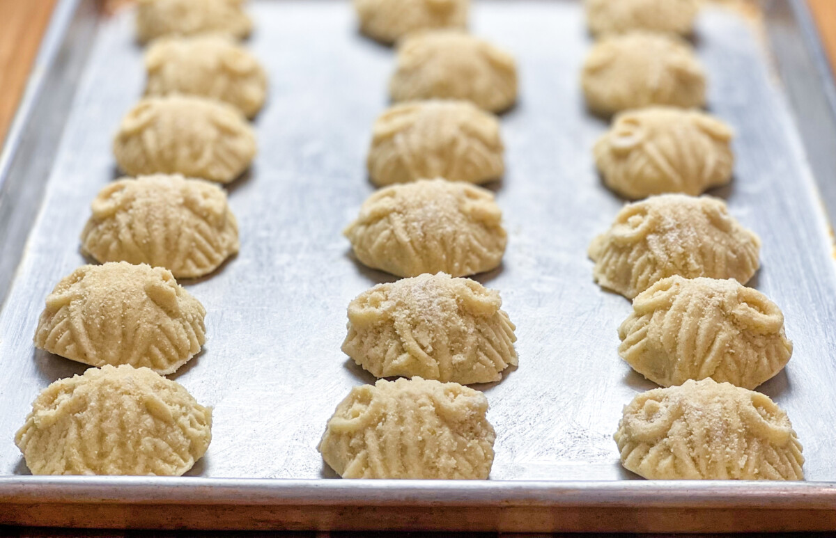 A photo showing a tray filled with perfectly formed Mammoul cookies, ready to be baked. The cookies are arranged in neat rows and are made with a sandy mixture of semolina, sugar, clarified butter, and yogurt, with various fillings such as walnut, date, or pistachio. The cookies are a tribute to the rich and flavorful culinary traditions of the Middle East and promise a delicious and satisfying treat.