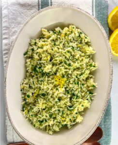 A serving bowl of lemon Greek yellow rice with fresh herbs on top.