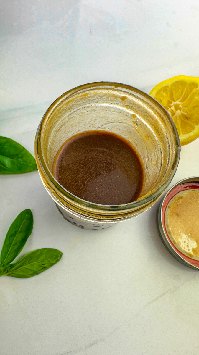 A small jar containing balsamic vinegar, olive oil, lemon juice, salt, and pepper whisked together to create a marinade.