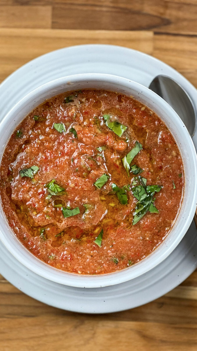 A vibrant bowl of homemade Gazpacho soup garnished with fresh basil.
