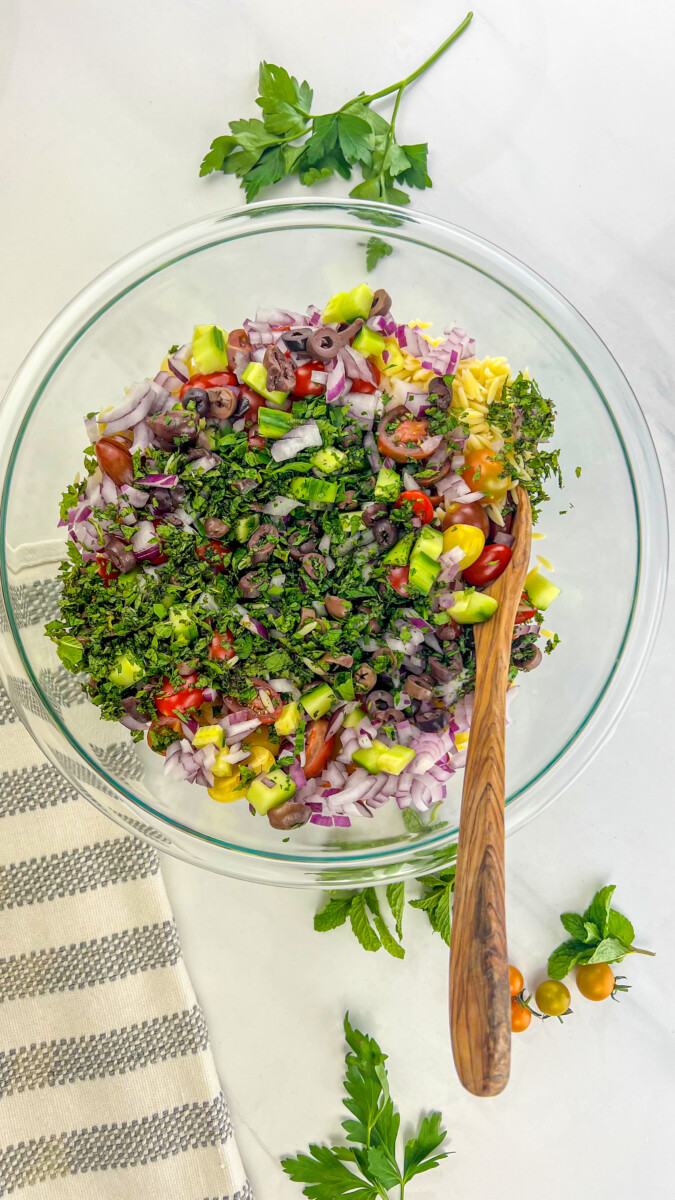 Freshly cut cherry tomatoes, diced cucumber, finely diced red onion, and sliced Kalamata olives for Greek Orzo Salad preparation.