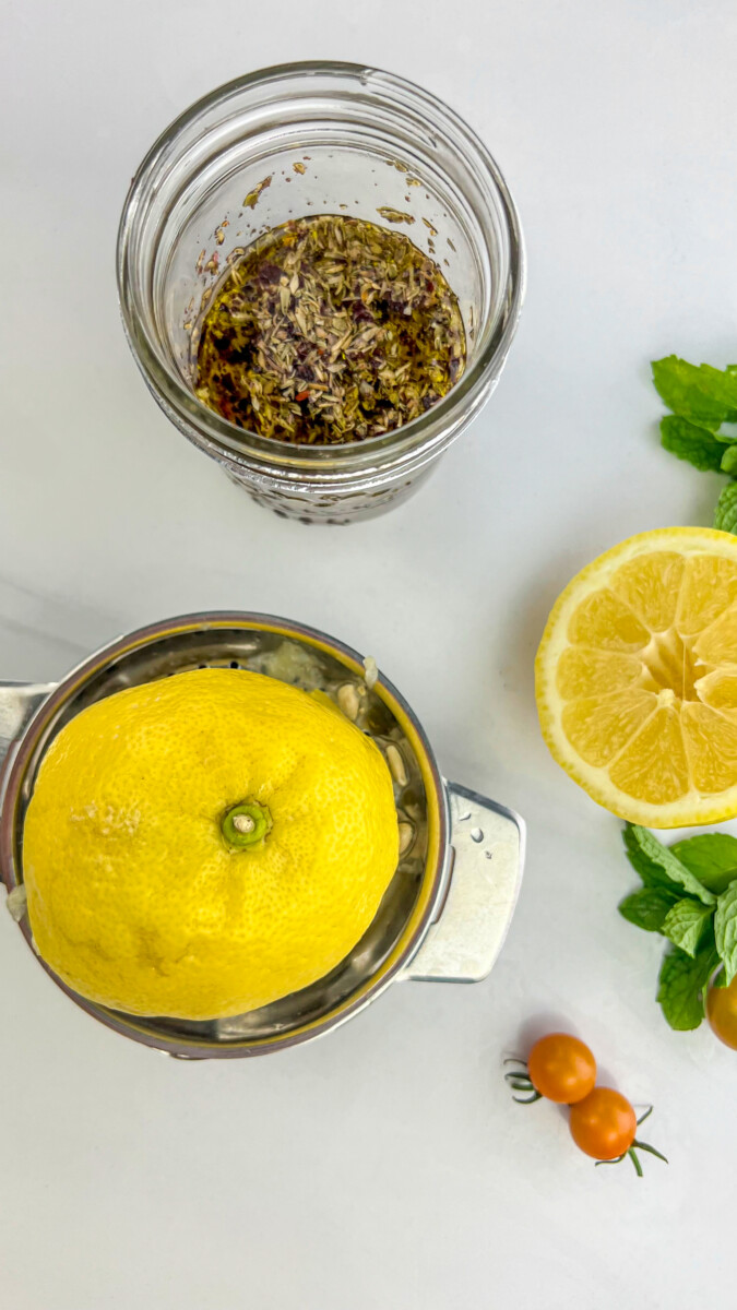 Ingredients combined in a small jar for Greek Orzo Salad dressing: olive oil, lemon juice, minced garlic, dried oregano, salt, and pepper.